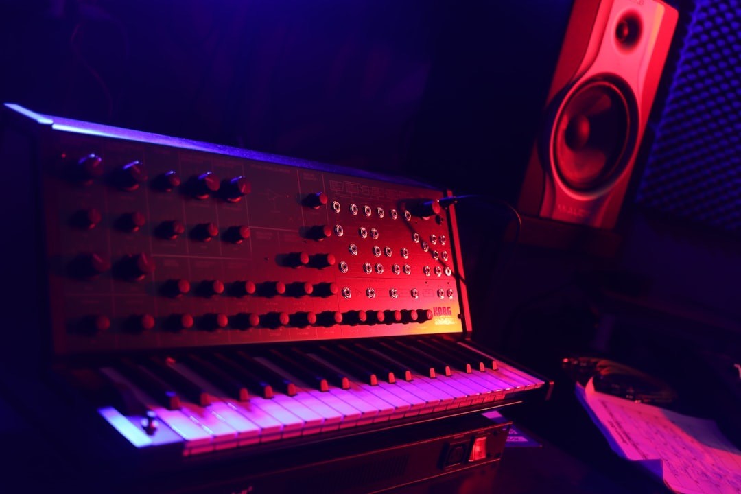 Image shows a synthesiser and speaker in a blue-pink lit studio